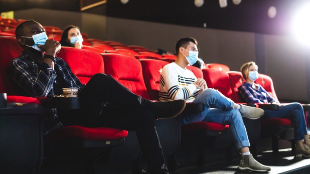 Besucher eines Kinos mit Mundschutz und Abstand zueinander.