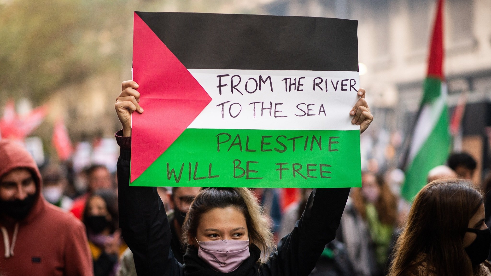 Demonstrantin hält ein Plakat hoch: "From the river to the sea, Palestine will be free"