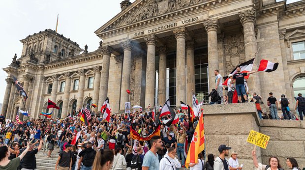 Teilnehmer der Demonstration in Berlin gegen die Corona-Maßnahmen stehen auf den Stufen zum Reichstagsgebäude, zahlreiche Reichsflaggen sind zu sehen.