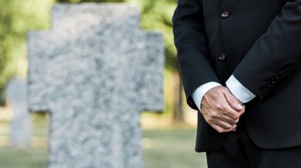Mann steht im schwarzen Anzug vor einem Grab