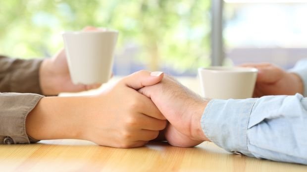 Paar hält sich die Hände und tauscht sich bei einer Tasse Kaffee aus (Symbol)