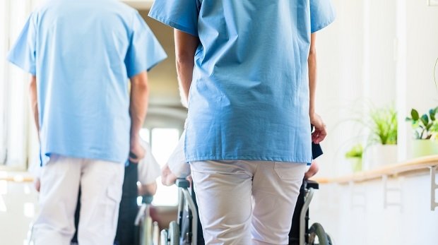 Zwei Pflegekräfte schieben einen Rollstuhl