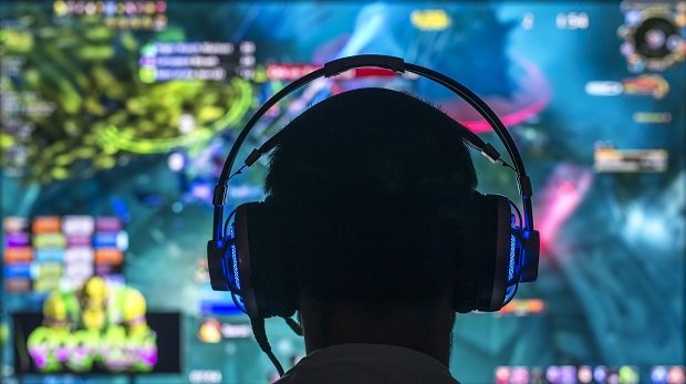 Person mit Headset vor Gaming-Monitor.