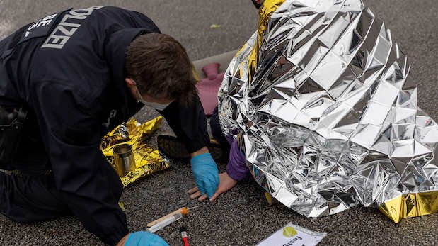 Ein Polizist löst mit Lösungsmittel Klebstoff, mit dem sich ein Aktivist festgeklebt hat. Klimaaktivisten der Gruppe „Aufstand der letzten Generation" sitzen auf der Fahrbahn Autobahn A100. (04.02.22)