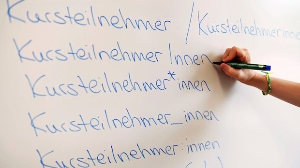 An einem an einem Whiteboard steht das Wort Kursteilnehmer in verschiedenen Gender-Schreibweisen.