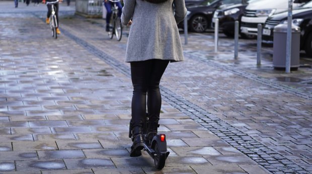 Frau auf E-Scooter mit Fahrrädern im Hintergrund.