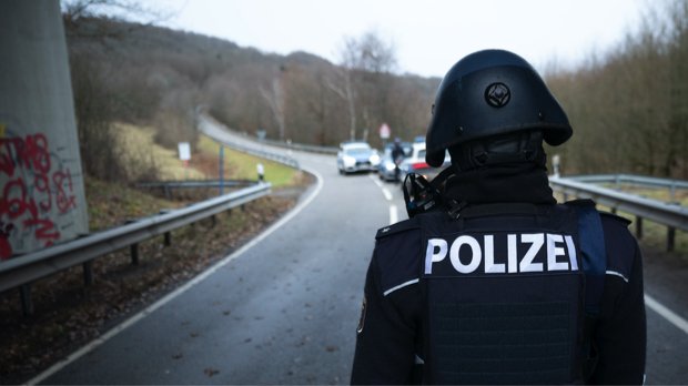 Polizeibeamte stehen an einer Absperrung an der Kreisstraße 22 rund einen Kilometer von dem Tatort, an dem zwei Polizeibeamte durch Schüsse getötet wurden.