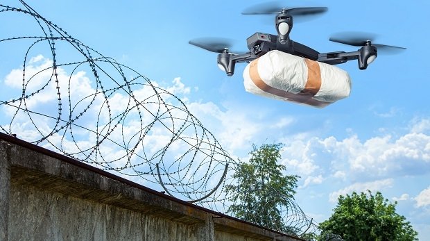 Drohne mit Paket vor Mauer mit Stacheldraht