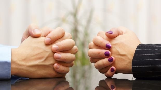Zwei Personen sitzen sich mit gefalteten Händen gegenüber