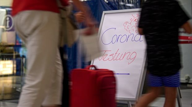 Reisende laufen an einem Aufsteller mit der Aufschrift "Corona Testung" vor einer Corona-Teststation für Urlaubsrückkehrer am Flughafen Dresden International vorbei.