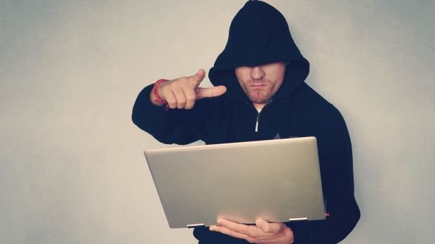 Maskierter Mann droht mit Laptop in der Hand