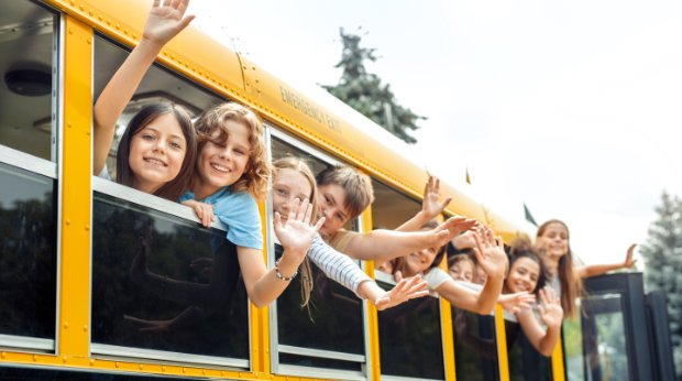Kinder winken aus dem Fenster eines Schulbusses