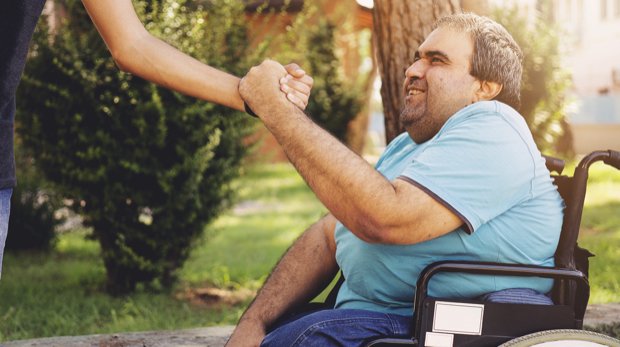 Ein Mann im Rollstuhl begrüßt seinen Betreuer im Park